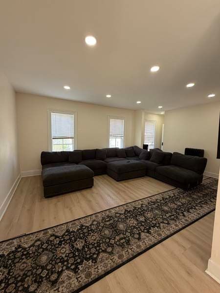 Modern living room with dark sectional sofa, recessed lights, windows, and patterned runner rug.