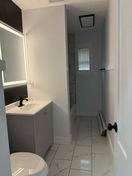 Small bathroom with gray vanity, toilet, white tile floor, and a hallway leading to a shower.