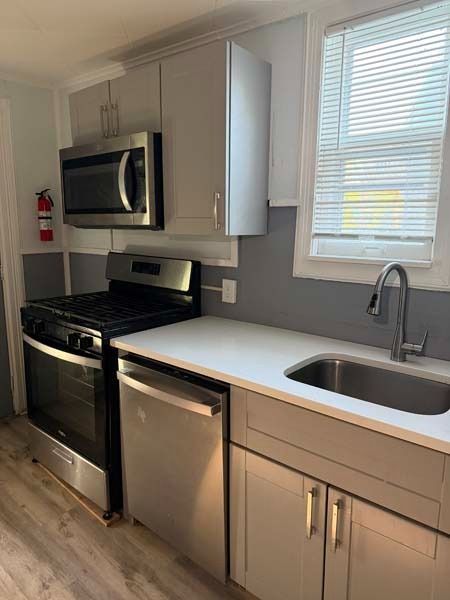 Small modern kitchen with stainless steel appliances, white cabinets, and a window over the sink.