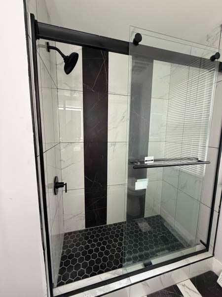 Modern glass shower enclosure with black fixtures, white tile walls, and hexagon tile floor.