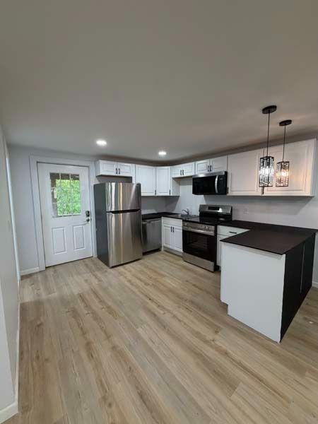 Modern kitchen with stainless steel appliances, white cabinets, and light wood flooring