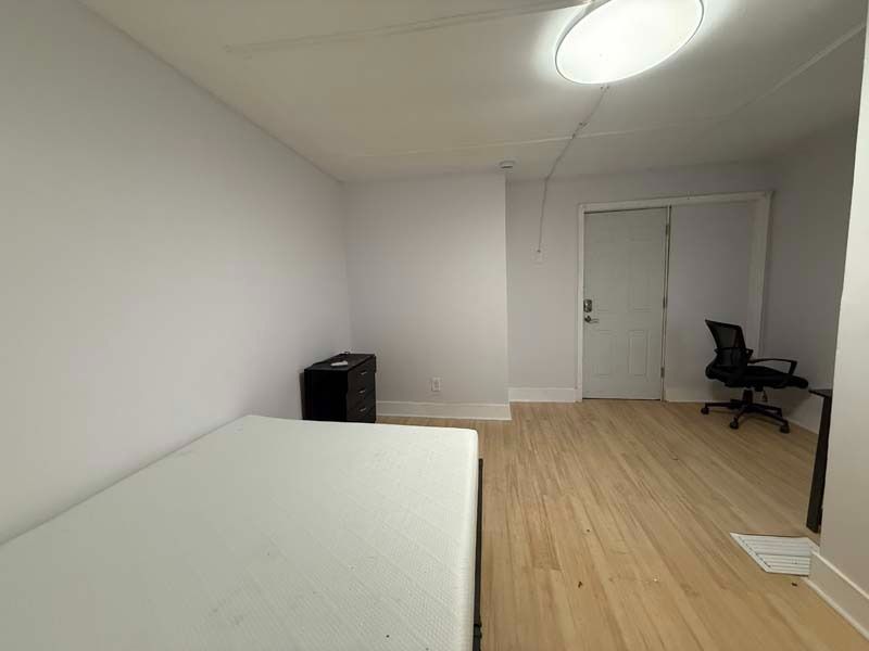 Empty bedroom with a bed, desk chair, dresser, and double doors on wood flooring
