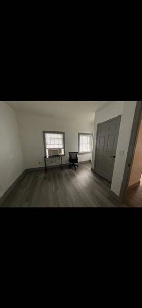 Small empty room with two windows, a chair by the wall, and a closet door on the right.