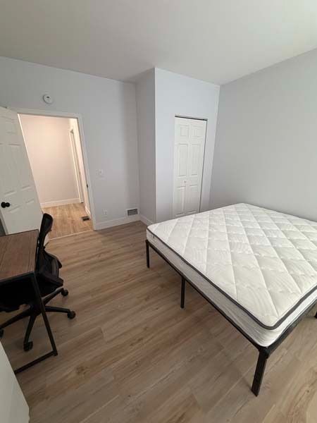 Sparse bedroom with a bed, office chair, closet, and open doorway on wood floors