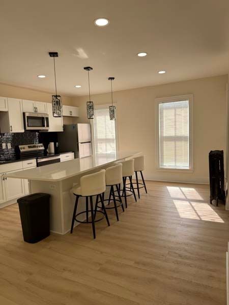Bright modern kitchen with white island, bar stools, and sunlight on wood floors