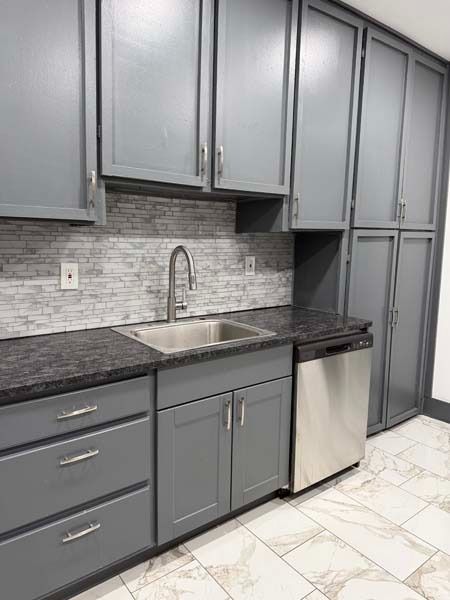 Modern kitchen with gray cabinets, black countertop, stainless sink, and tiled backsplash