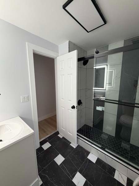 Modern bathroom with black tile floor, glass shower, white vanity, and an open door.