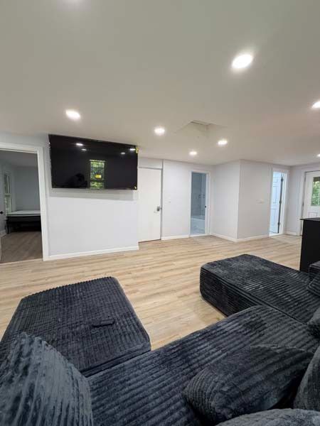 Modern living room with dark sectional sofa, wall-mounted TV, wood floors, and recessed lighting