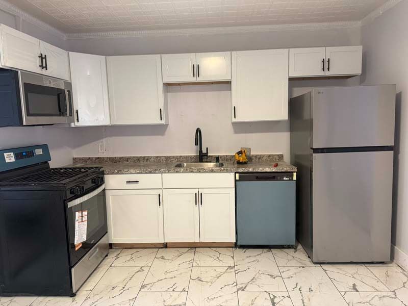 Small kitchen with white cabinets, granite countertops, black stove, microwave, dishwasher, and stainless steel fridge.