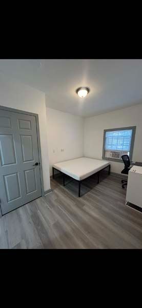 Small empty room with gray door, window, desk, and office chair on wood-look flooring