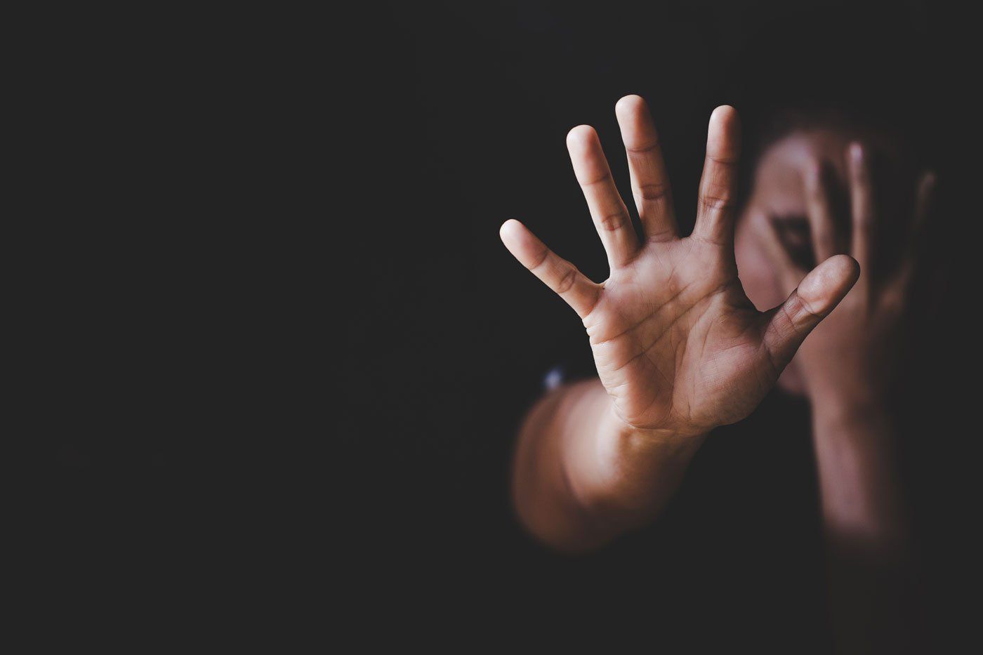A person reaching out with an open hand, palm facing forward, against a dark, shadowy background.