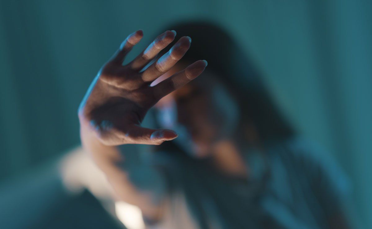 A close-up of a hand held forward in a gesture of blocking or defense, with the person behind out of focus in blue light.
