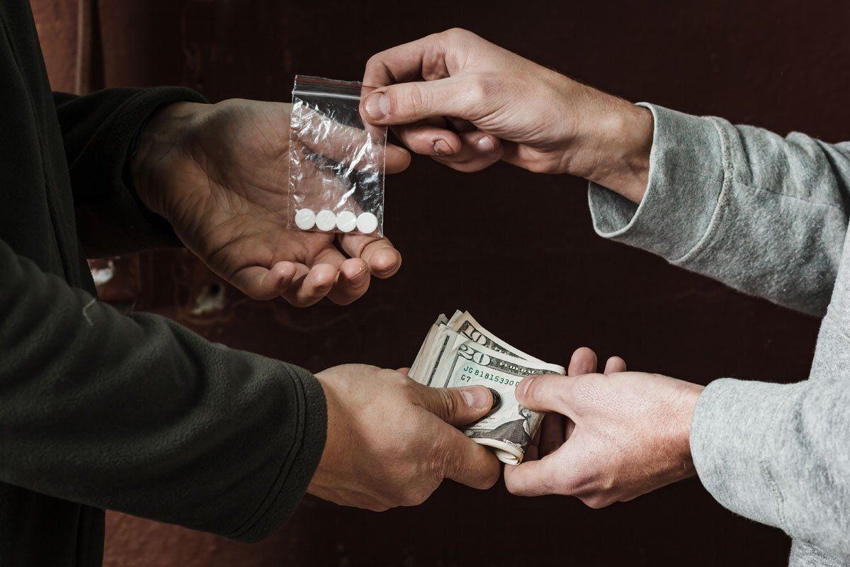Two individuals exchanging a small plastic bag of white pills for a stack of US currency.