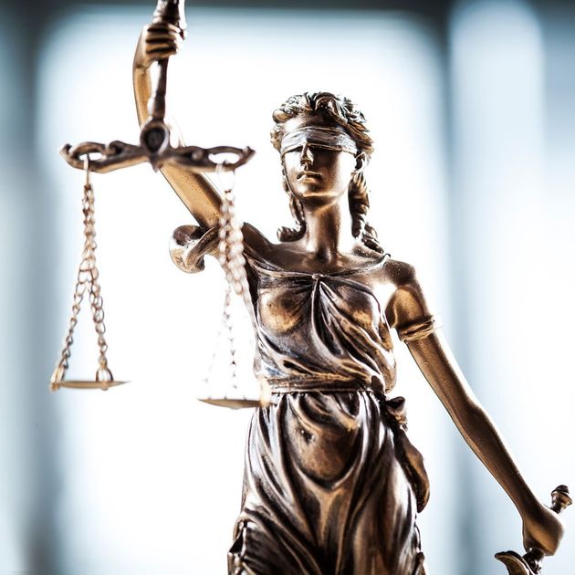 Bronze statue of Lady Justice wearing a blindfold and holding a scale and sword against a blurred, bright background.