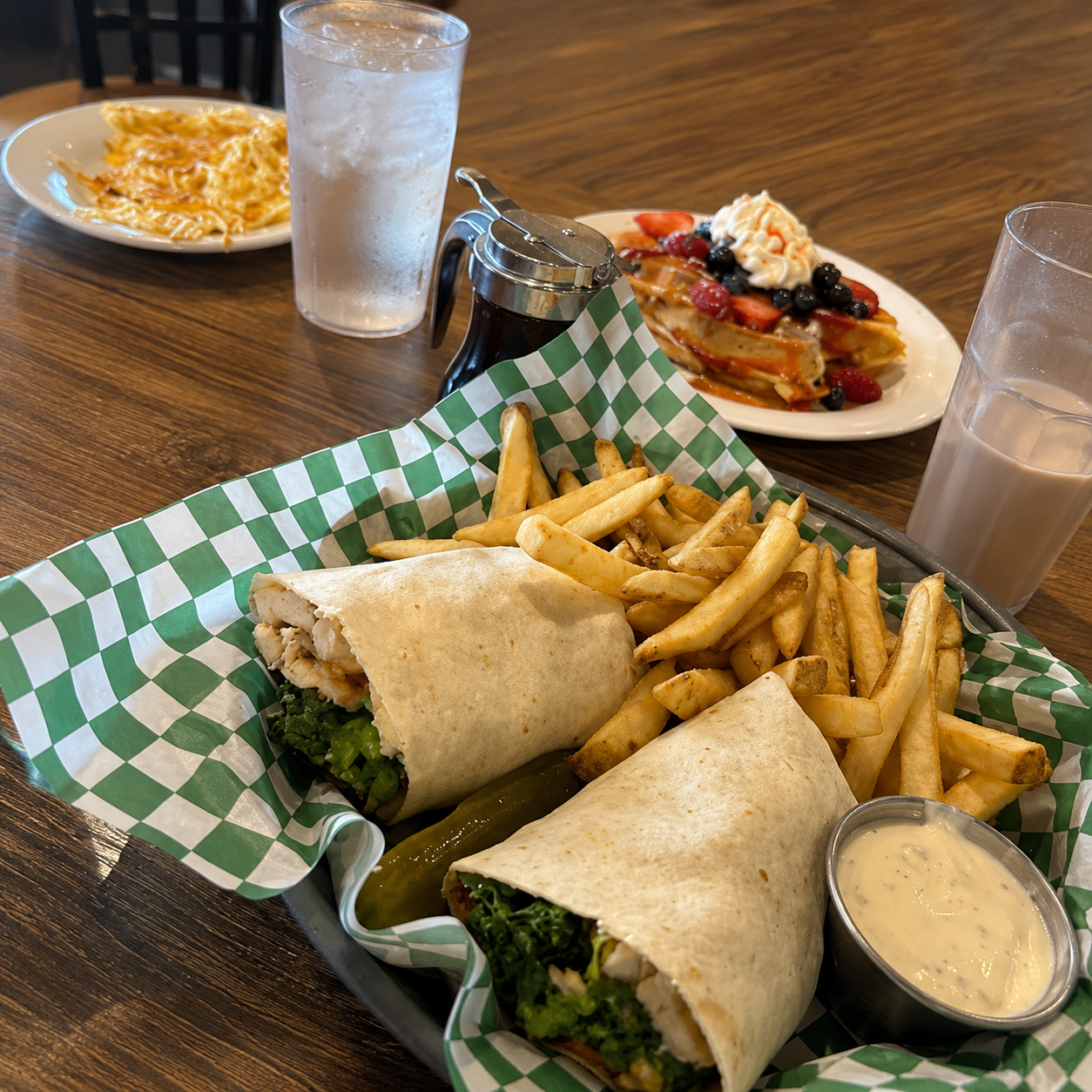 Two wrap sandwiches with fries and dipping sauce on a checkered tray at a restaurant table.