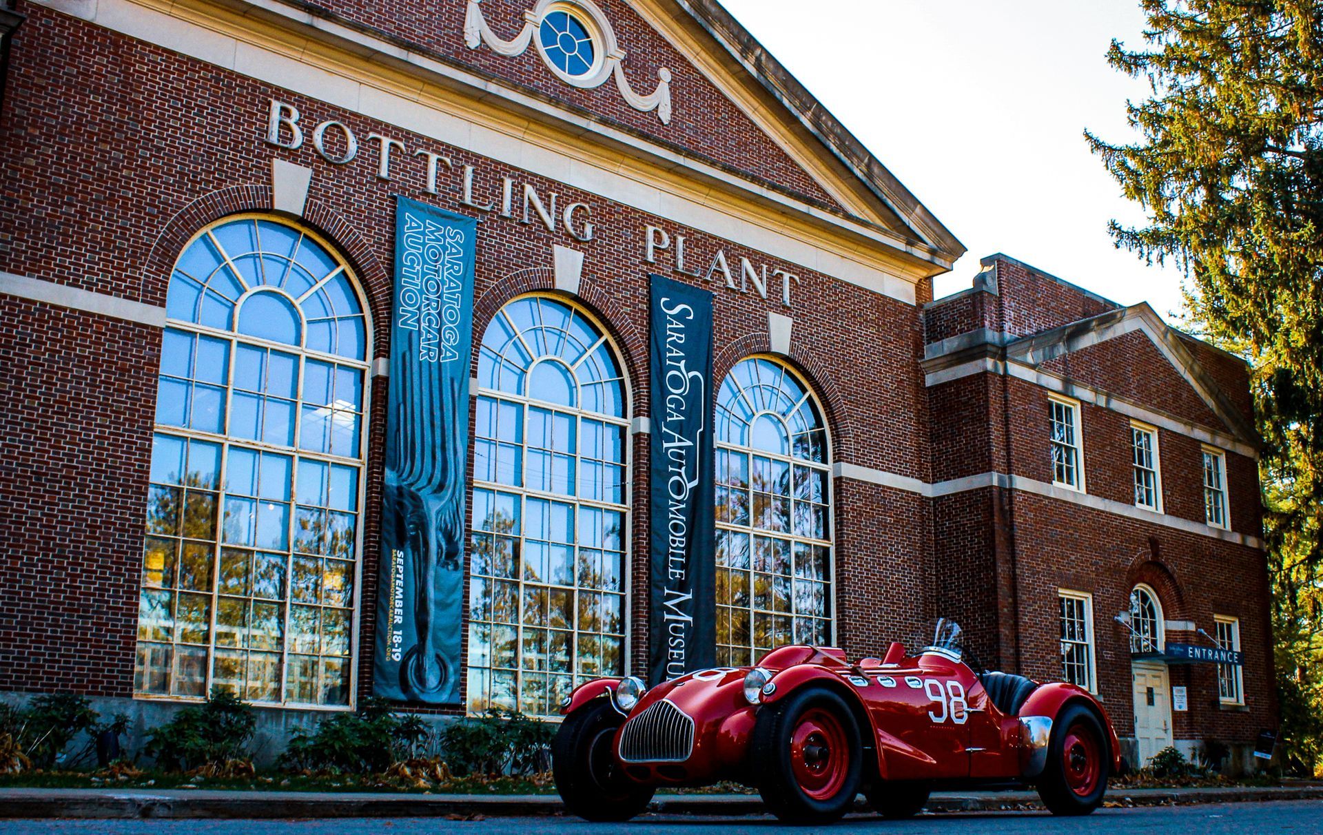 Red vintage race car parked in front of a brick building labeled 