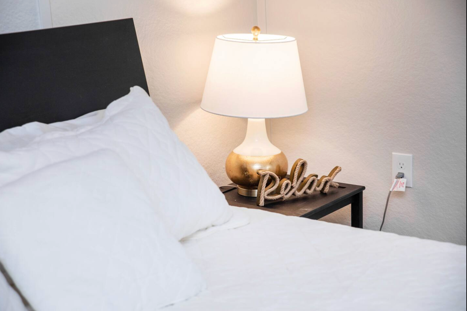 Bed with white bedding and pillows, nightstand with lamp and