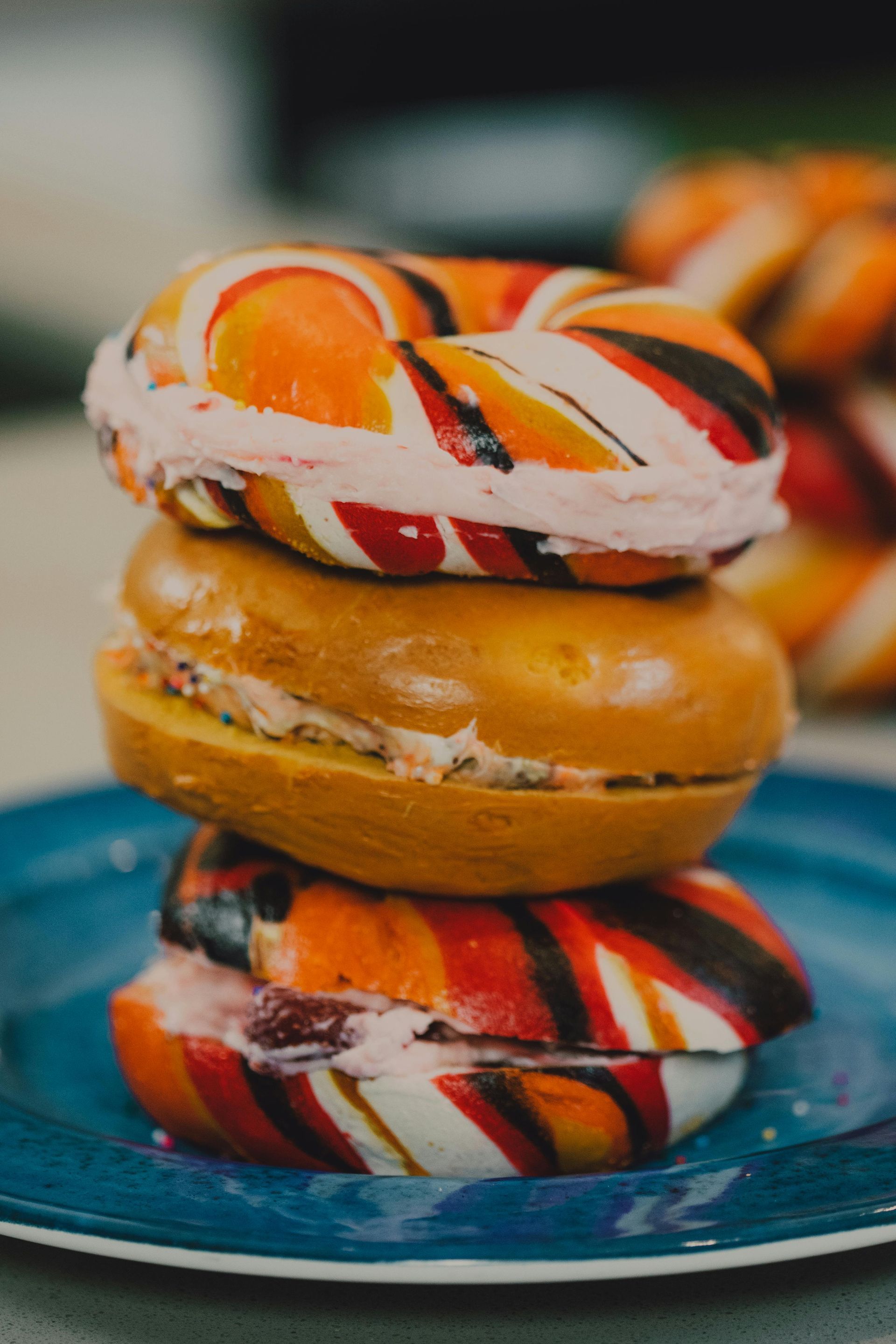 Three colorful bagels stacked with cream cheese on a blue plate.