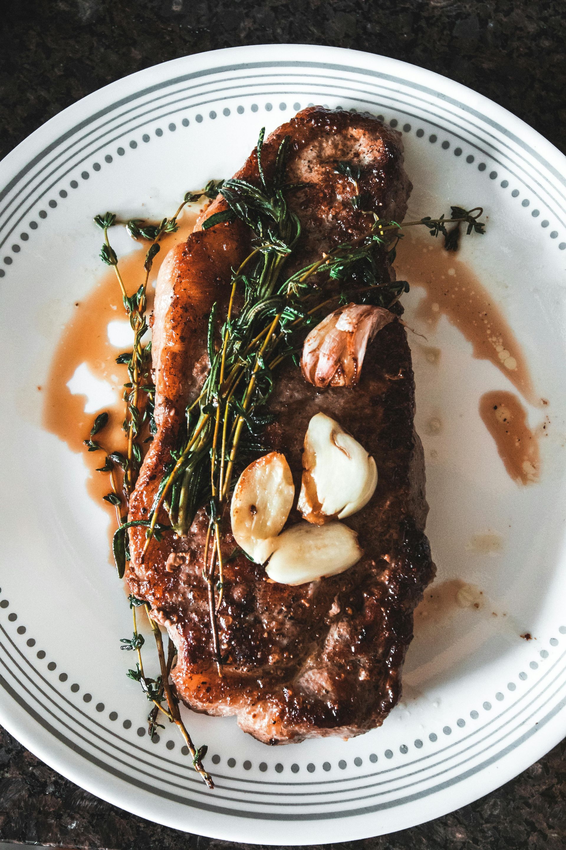 Seared steak with garlic and thyme on a white plate.