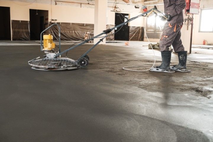 Worker using a floor-polishing machine on a wet concrete floor indoors