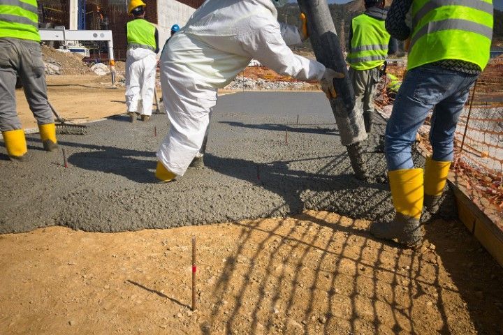 Workers in reflective vests pouring concrete at a construction site around rebar mesh