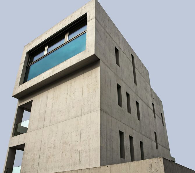 Modern concrete building with a large blue-tinted window against a clear sky
