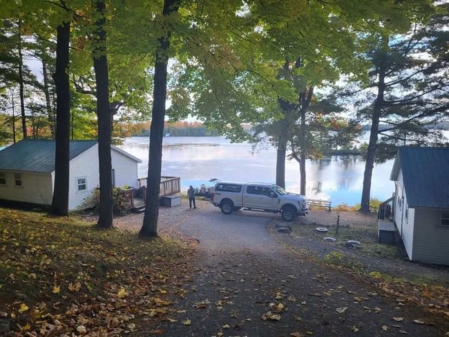 Leafy lakeside driveway with parked truck, small cabins, and mist over the water