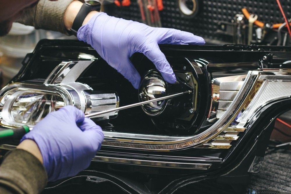 A Person Wearing Purple Gloves is Working on a Car Headlight — Ravenshoe Auto Electrical In Ravenshoe, QLD