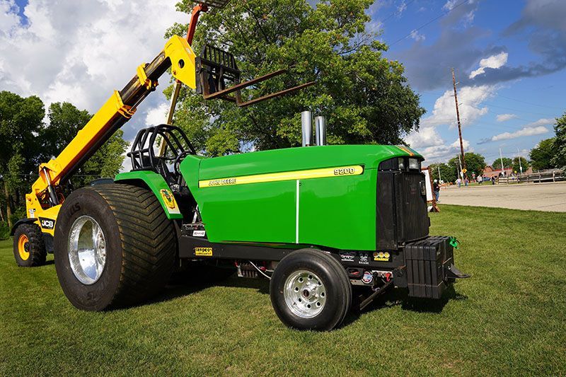 A bright green John Deere tractor-pulling vehicle parked on grass with a yellow telehandler lift arm extended overhead.