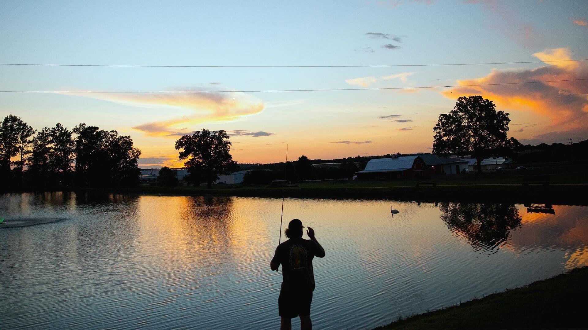 A man is fishing in a lake at sunset.