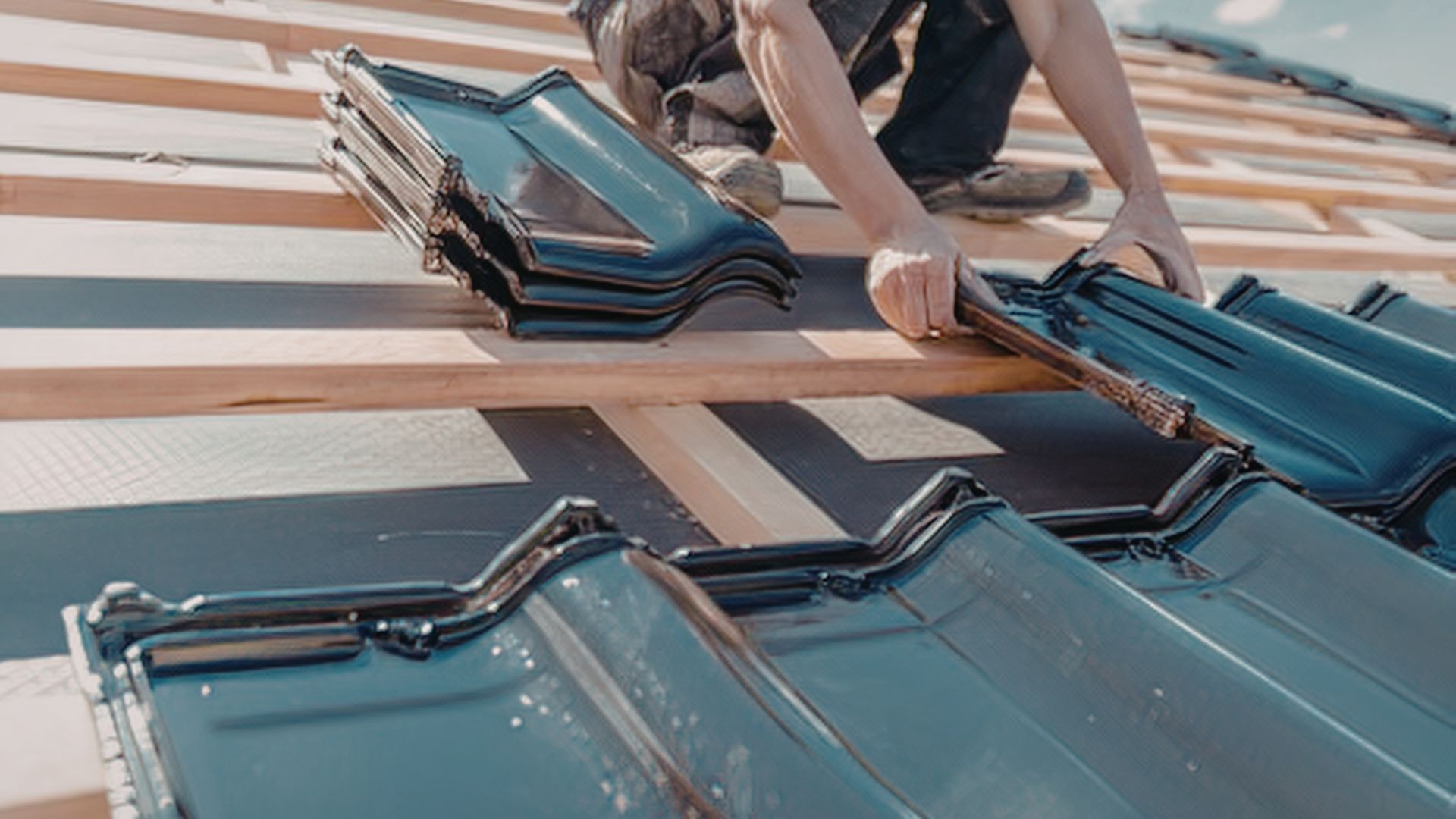 Hands installing blue solar roof tiles on a sloped roof