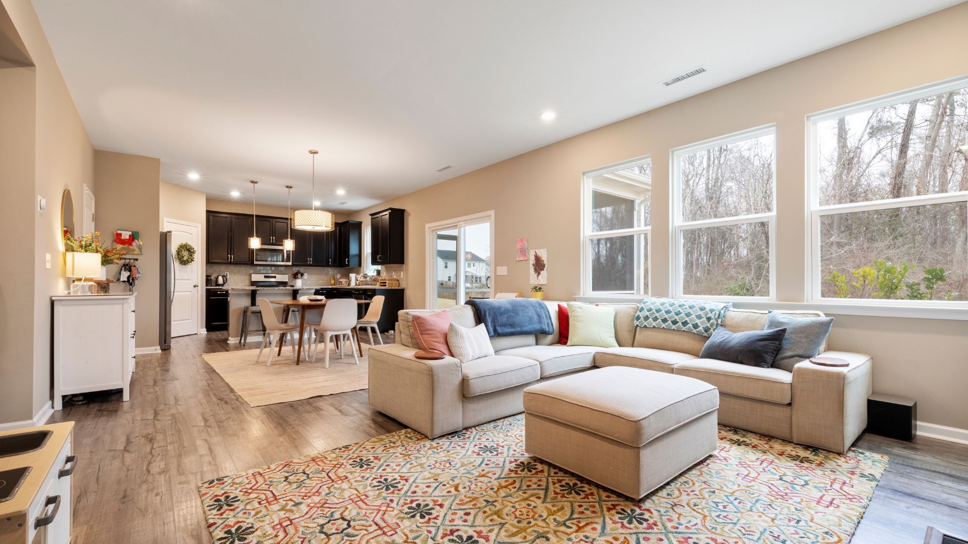 Bright open living room with beige sectional, colorful rug, and large windows overlooking trees