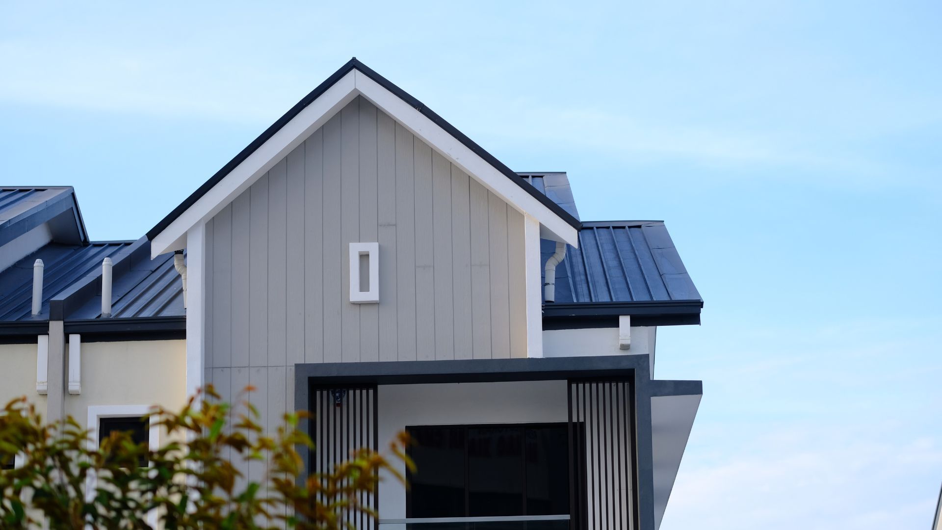 Modern house exterior with gray siding, black roof, and blue sky background