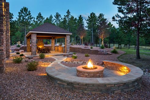 A fire pit in a backyard with a gazebo in the background.