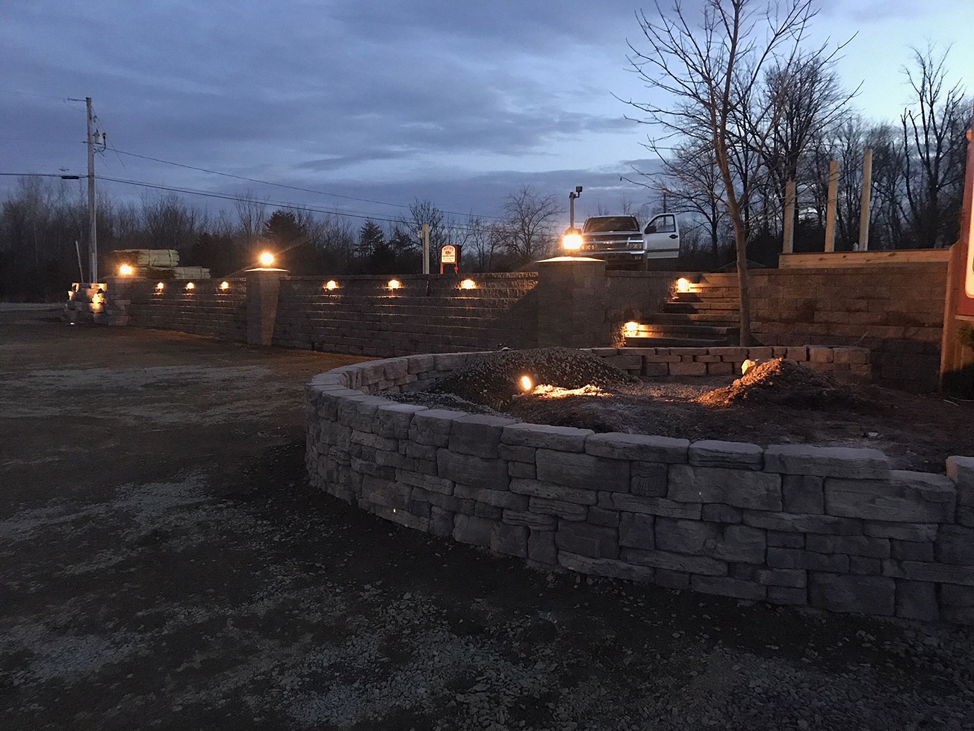A stone wall is lit up at night in a parking lot