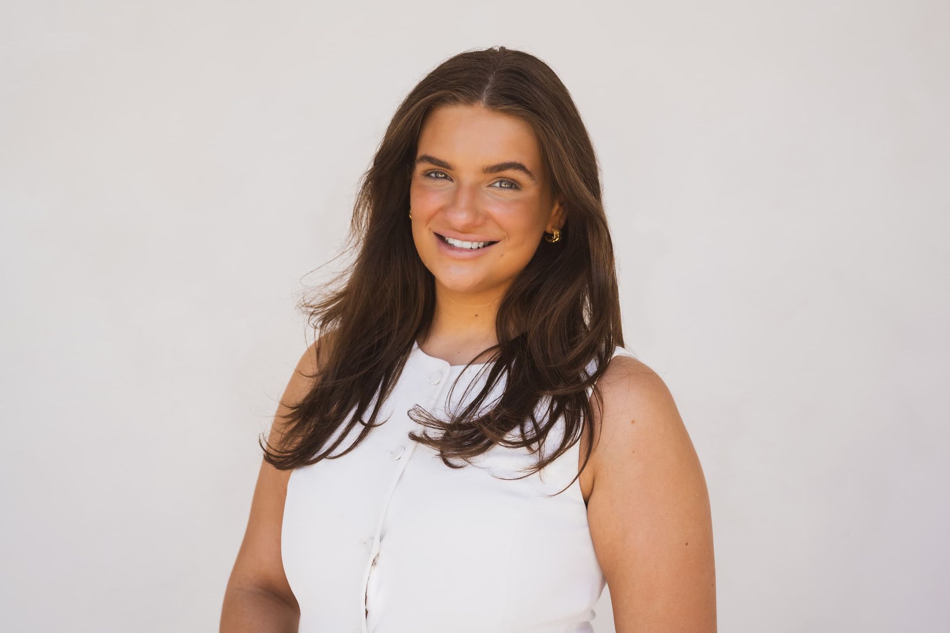 A woman in a white tank top is smiling for the camera.