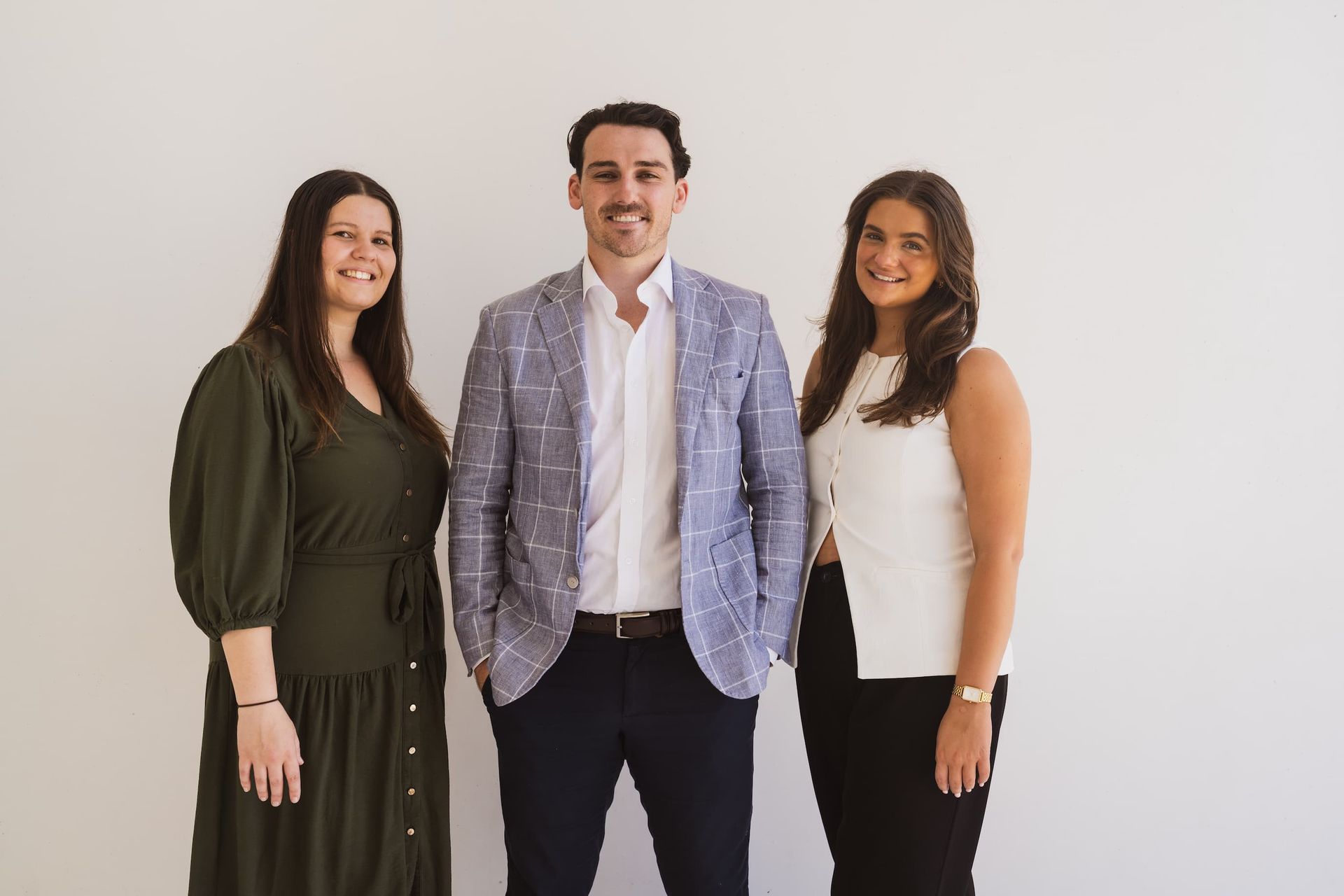 A man and two women are standing next to each other in front of a white wall.