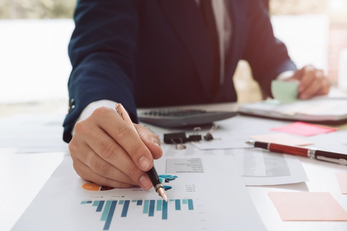 A man in a suit is writing on a piece of paper with a pen.