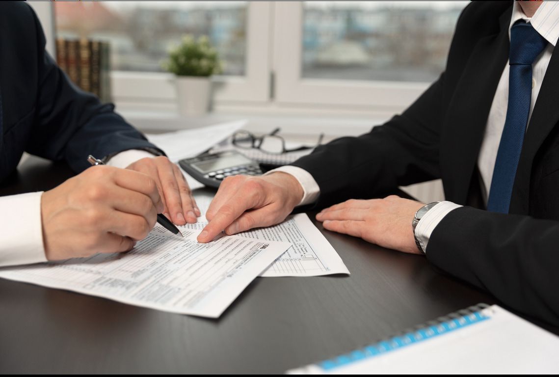 Two men are sitting at a table signing a document.