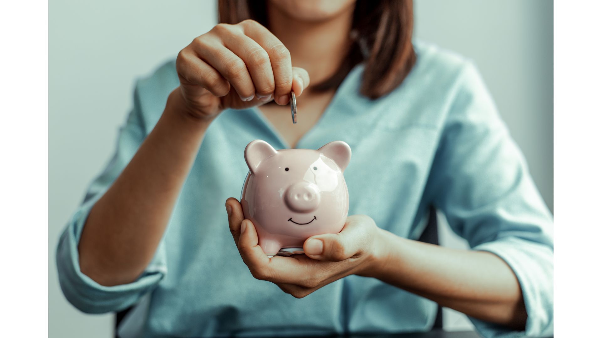 A woman is putting a coin into a piggy bank.