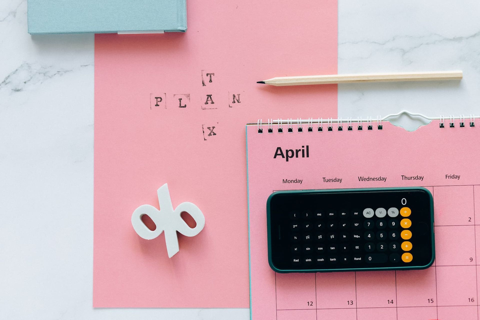 A pink calendar with a cell phone , calculator , and pencil on a table.