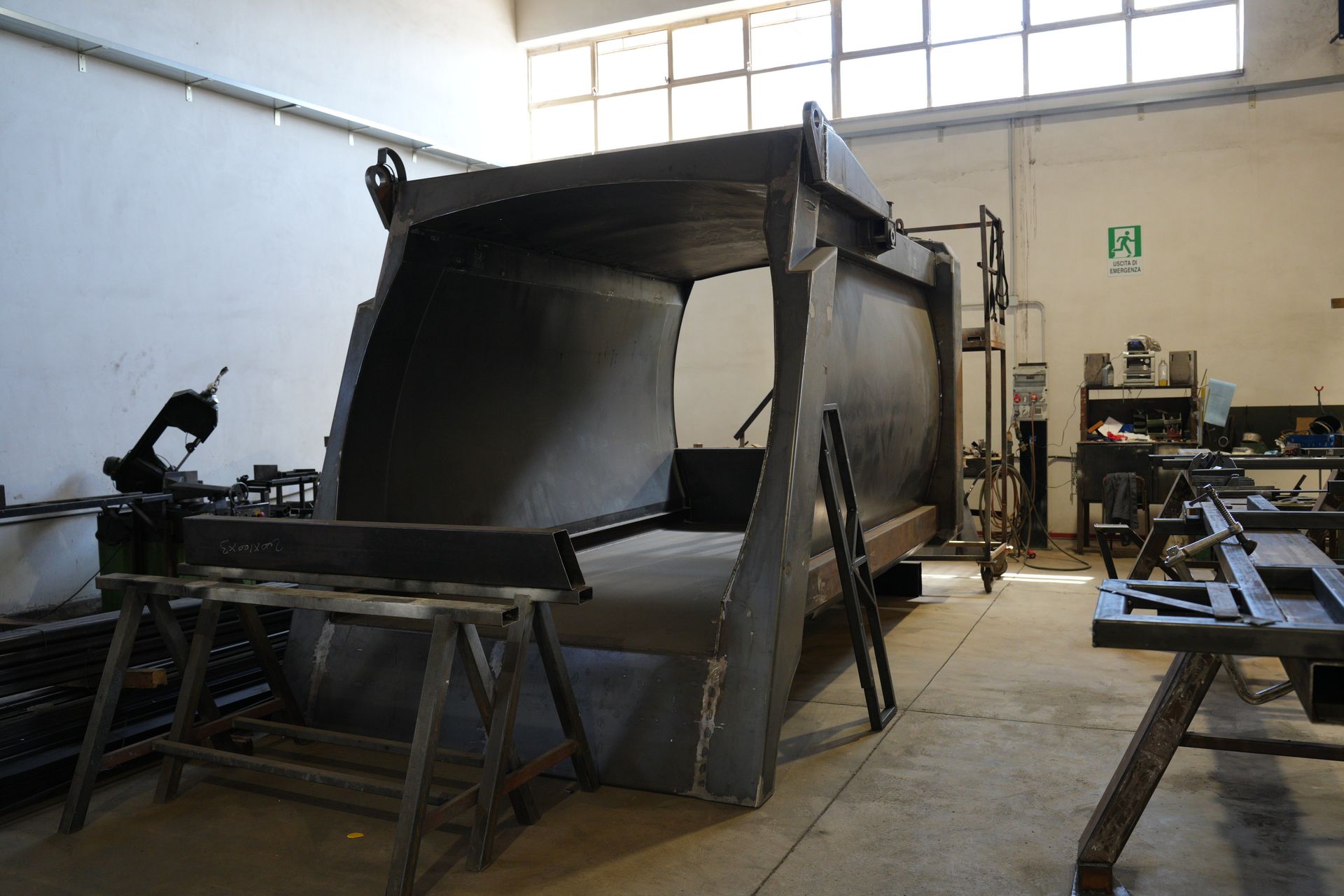 Grande macchinario industriale o stampo in un'officina, circondato da tavoli e utensili metallici.