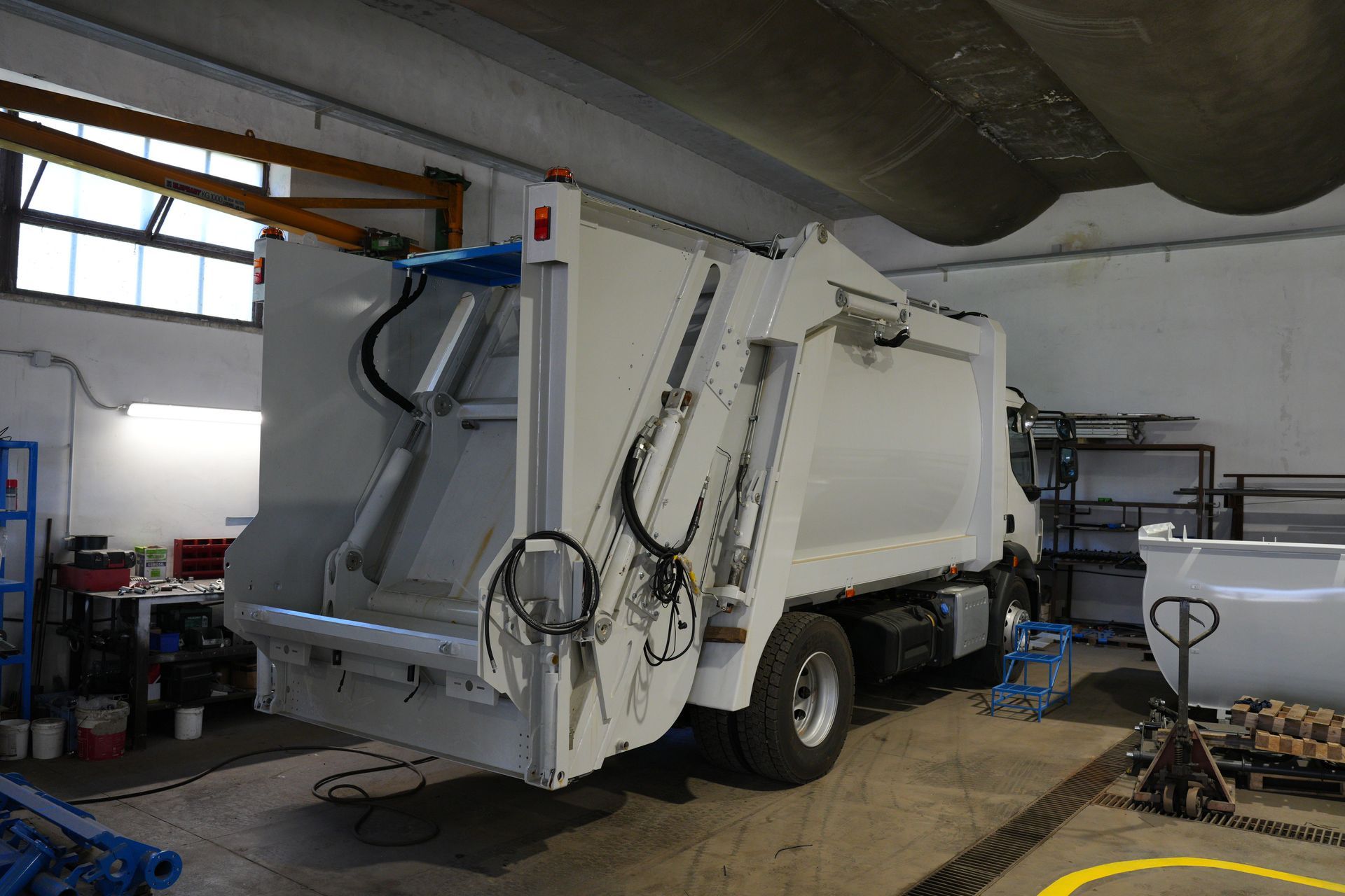 Camion della spazzatura bianco all'interno di un garage, visto da dietro con la tramoggia aperta e sollevata.
