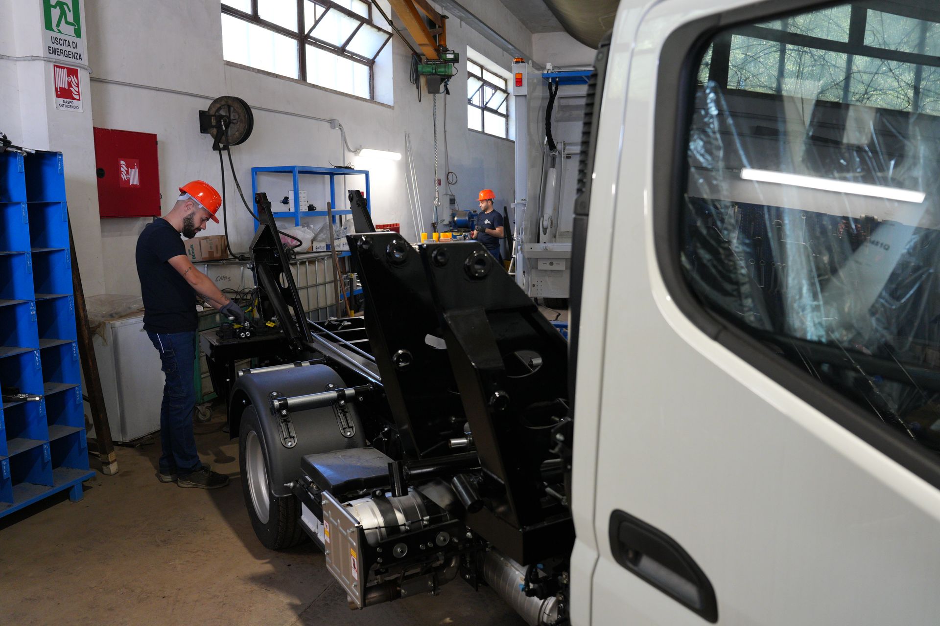 Un meccanico lavora su un telaio di camion nero in un'officina, con una cabina di camion bianca in primo piano.
