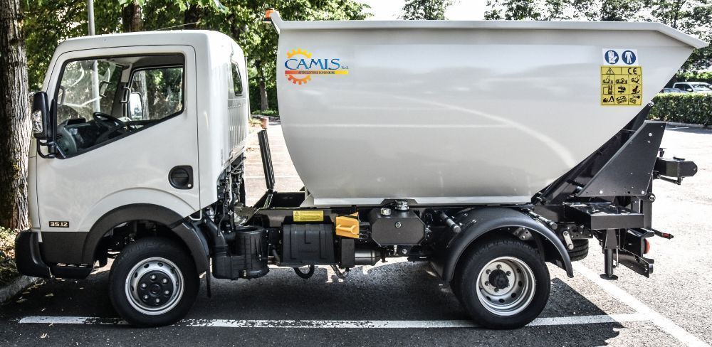 Camion della spazzatura bianco e grigio parcheggiato su una strada alberata