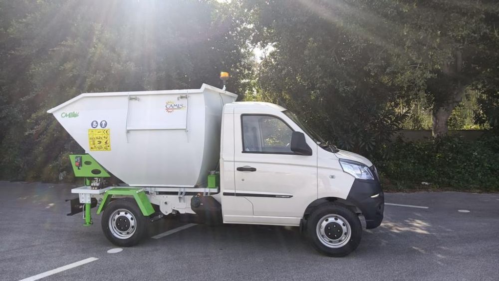 Un camioncino bianco parcheggiato su una strada, illuminato da una luce solare intensa, con degli alberi sullo sfondo.
