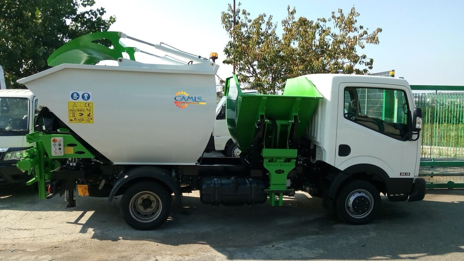 Camion betoniera bianco e verde parcheggiato su un terreno sterrato sotto un sole splendente
