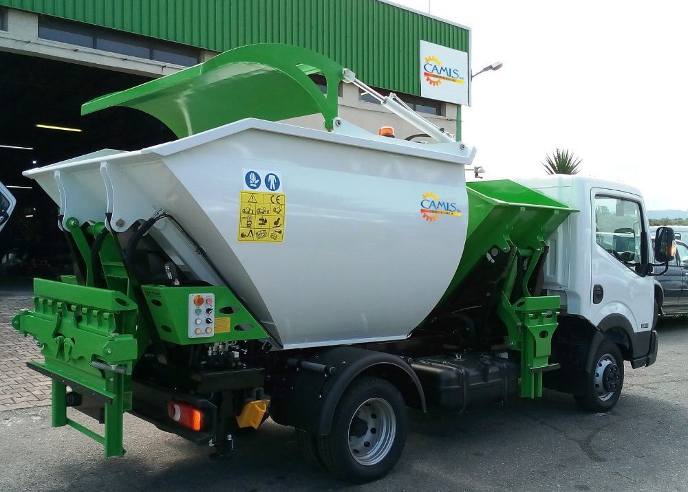 Camion industriale bianco con una grande tramoggia verde e bianca parcheggiato fuori da un magazzino