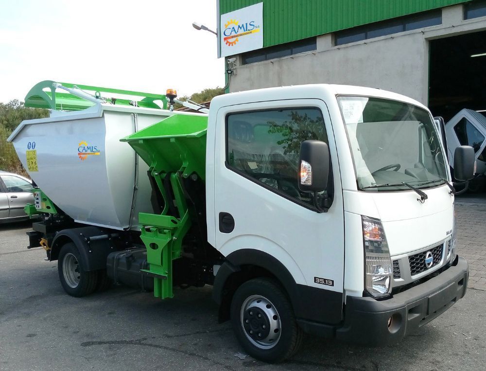 Camion della spazzatura con cabina bianca e cassone posteriore verde parcheggiato fuori da un edificio