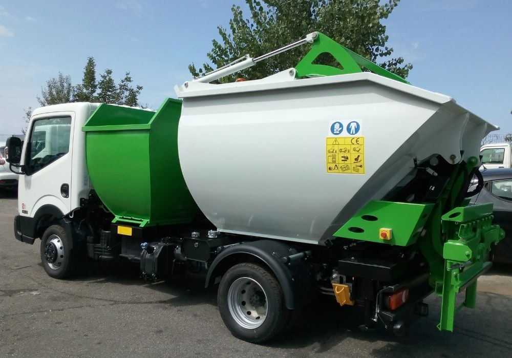 Camion della spazzatura verde e bianco con un grande cassonetto parcheggiato all'aperto in una giornata di sole.